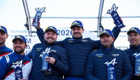 Groupe de participants sur un podium tenant des trophées Alpine A290, portant des vestes et casquettes officielles. Plusieurs trophées affichent les mentions “Pilote”, “Copilote” et “A290”.