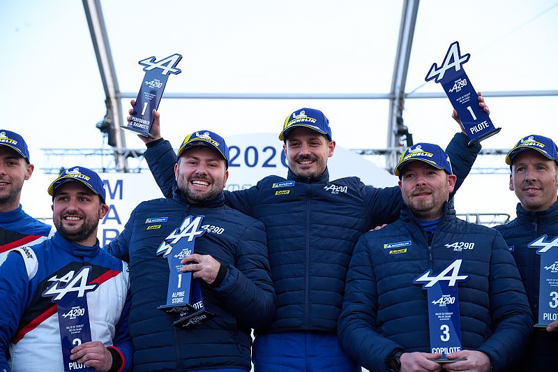 Groupe de participants sur un podium tenant des trophées Alpine A290, portant des vestes et casquettes officielles. Plusieurs trophées affichent les mentions “Pilote”, “Copilote” et “A290”.